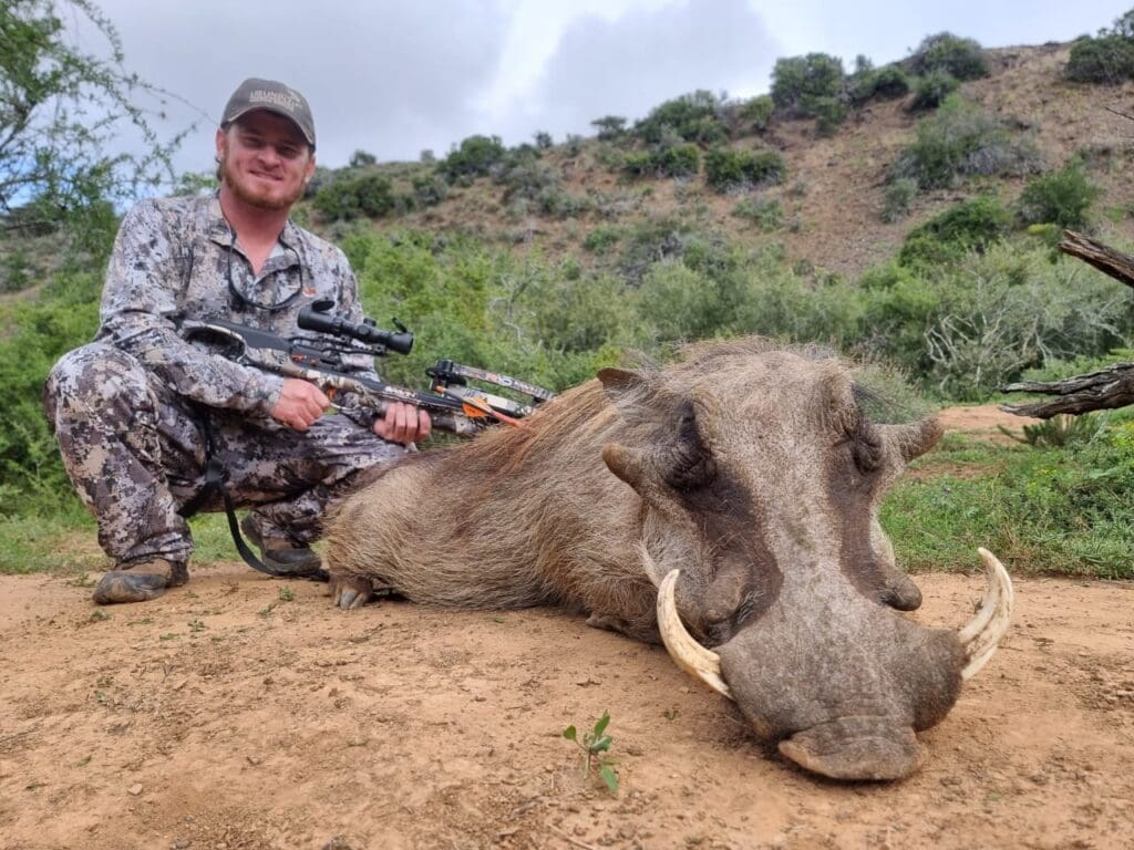 Hunter kneeling next to a warthog after a successful hunt in Africa.